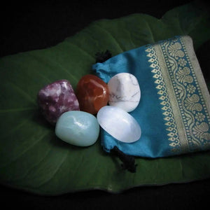 Luxurious Back Pain Tumbles collection featuring smooth healing stones on a vibrant green leaf, with a silk pouch holding Lepidolite, Amazonite, Howlite, and Selenite, perfect for promoting inner balance and well-being.